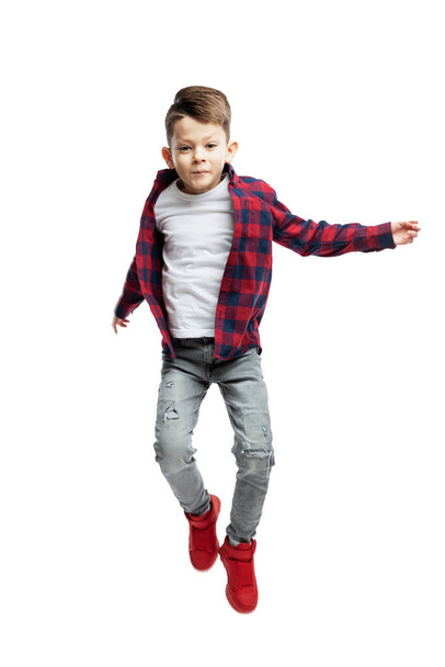 A 7-year-old boy in jeans, a white T-shirt and a red shirt is jumping. Isolated on white background. Vertical. - Fotografie, Obrázek