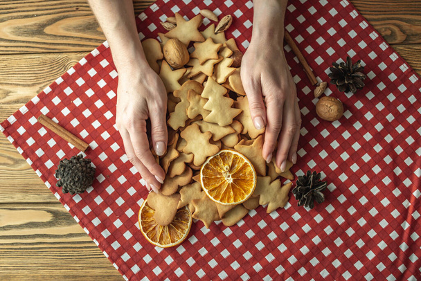 Woman's hands are holding homemade cookies on the red tablecloth on a wooden table. Concept of a festive atmosphere and cozy. Top view. - Photo, image