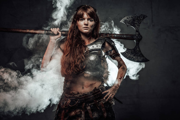 Mujer seria vikinga con hacha en fondo oscuro brumoso - Foto, Imagen