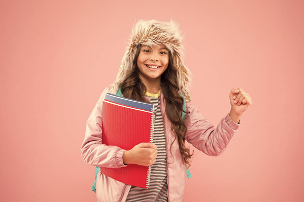 Catch me at my best. schoolgirl carry backpack and books go home. no more exams. small happy girl earflap hat. back to school. winter holiday. kid warm clothes pink background. pupil daily life - Photo, image