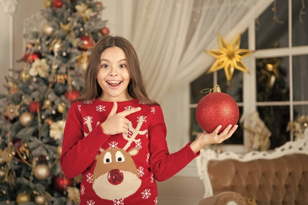 El rojo es mi favorito. Decoración de atributos navideños. Niña cerca del árbol de Navidad. El niño celebra la Navidad en casa. Tradiciones invernales. Adorable niño emocionado usar suéter de Navidad. Concepto tienda de regalos - Foto, Imagen