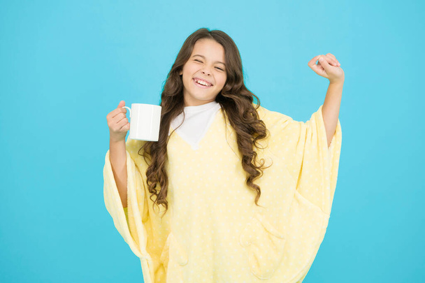 Wellbeing concept. Little girl with long hair. Feeling comfy. Adorable child on turquoise background. Comfy outfit for weekend rest at home. Comfy style. Kid wearing soft poncho drinking tea - Photo, image