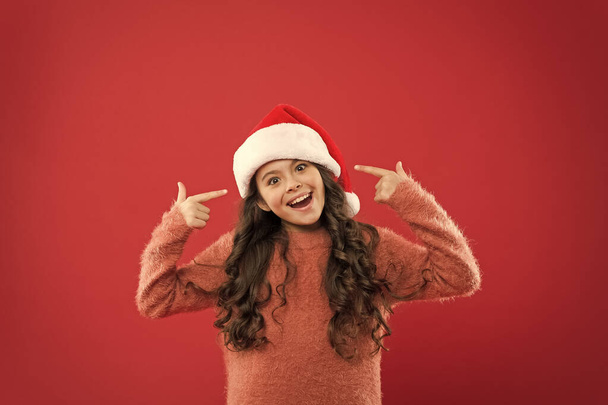 Adorable girl with long curly hair wear santa claus hat red background. Counting days till christmas. Christmas party. Christmas holiday invitation. Positivity concept. Good mood. Winter traditions - Photo, Image