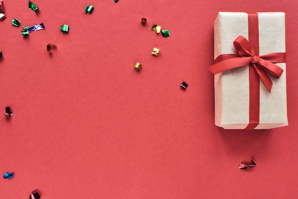 Рождественская композиция Подарок с красной лентой и конфетти украшения на пастельной бумаге красочный фон. Рождество, зима, новогодние праздники. Плоская кладка, вид сверху, копировальное пространство. - Фото, изображение