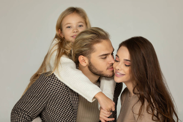 Happy father, daughter and mother embracing together in front of grey background. - Foto, Imagem