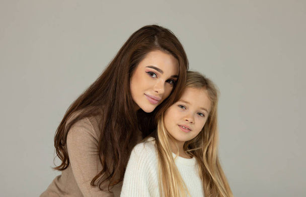 Charming little girl and her beautiful young mom hugging and smiling on grey background. Happy family. - Valokuva, kuva