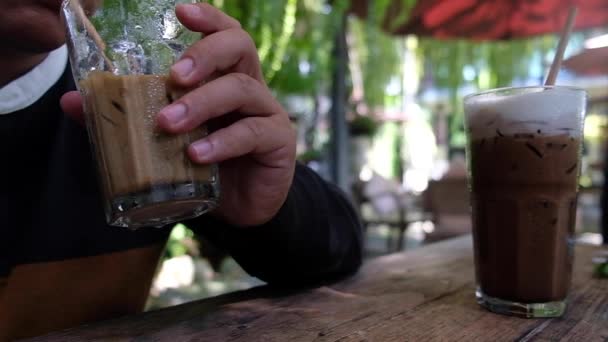 Mladý muž pije sklenici ledové kávy z papírové slámy v kavárně. Zpomalený záběr - Záběry, video