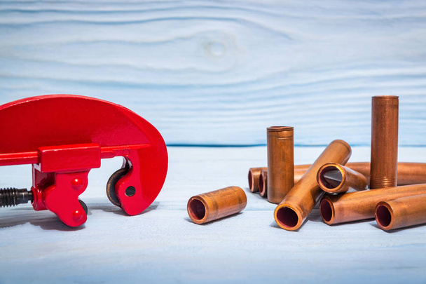 Cortador de tuberías rojo y tubos de cobre con conectores para reparaciones de fontanería en tableros de madera azul. - Foto, imagen