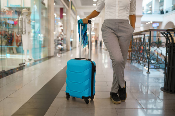 Woman with suitcase poses at the showcase in mall. Female traveler with luggage in shopping center, passenger with bag in tax free market. Girl with baggage - 写真・画像