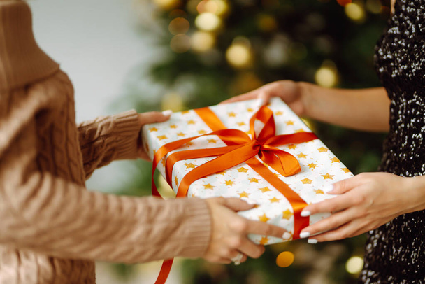 Gives the gift. Exchanging the christmas presen. Young woman gives a gift in a box. Winter holiday, New Year, celebration, birthday concept. - Zdjęcie, obraz