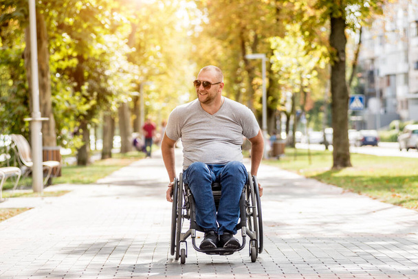 Ένας ανάπηρος με αναπηρική καρέκλα περπατάει στο δρομάκι του πάρκου. - Φωτογραφία, εικόνα