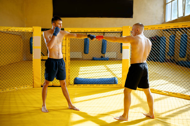 Hombres luchadores MMA manos con vendajes rojos y azules, jaula y gimnasio interior en el fondo. Hombres musculares en el ring, entrenamiento de combate, concepto de artes marciales - Foto, Imagen