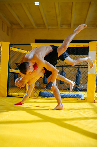 Dois lutadores de MMA lutam em uma gaiola no ginásio. Homens musculosos no ringue, treino de combate, treino de artes marciais, competição ou sparring - Foto, Imagem