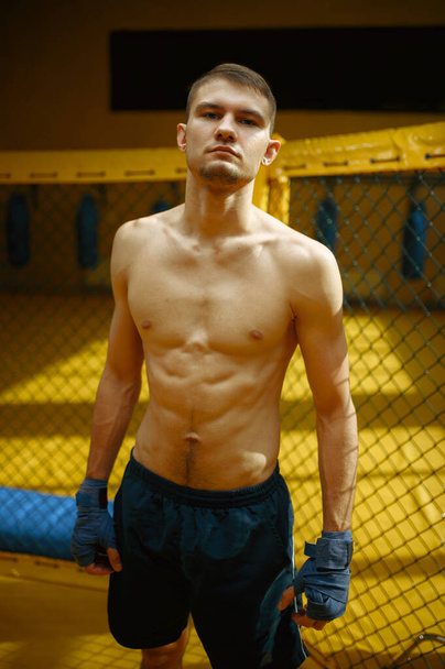 Combatiente masculino MMA de pie en una jaula en el gimnasio. Hombre musculoso en el ring, entrenamiento de combate, entrenamiento de artes marciales - Foto, Imagen