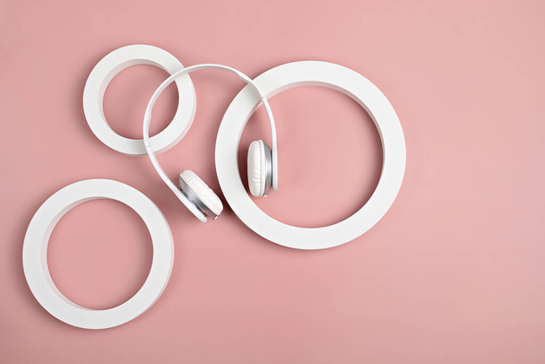White wireless headphones and circles on pink background. Product in abstract setting concept. Flatlay, top view - Photo, Image