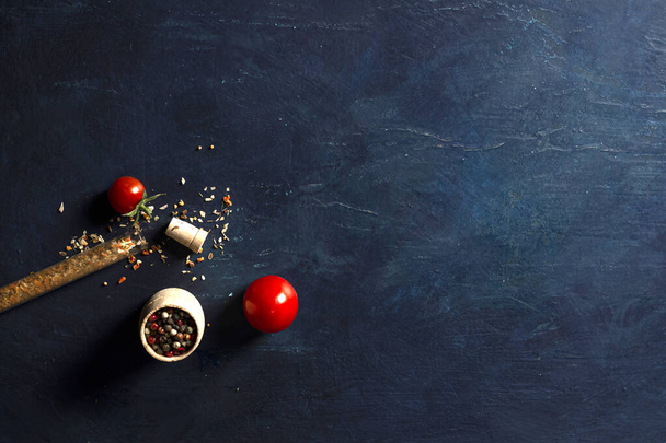 Spices, red and black peppercorns in a saucer with herbs and tomatoes. On a blue background. Place for text. - Фото, изображение