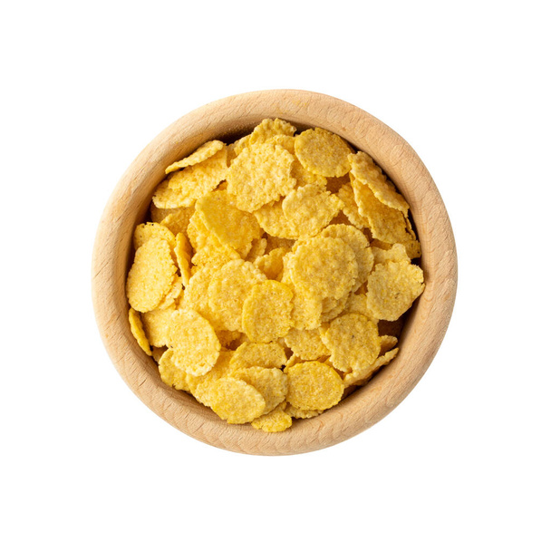 Yellow corn cereal for breakfast in round wooden bowl isolated on white background. Pile of crispy corn flakes, cornflakes or cereals top view - Photo, Image