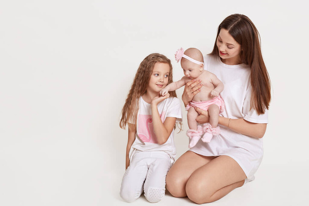 Happy mother and her two daughters posing isolated over white background. Mommy looks at her infants with great love. Copy space for your advertisement. - 写真・画像
