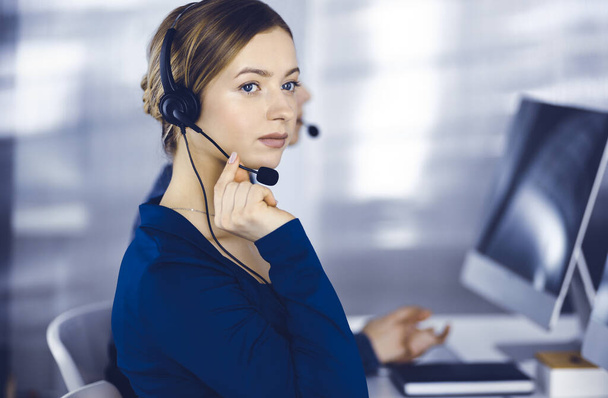Two busineswomen have conversations with the clients by headsets, while sitting at the desk in a modern office. Diverse people group in a call center. Telemarketing and customer service - Foto, Imagem