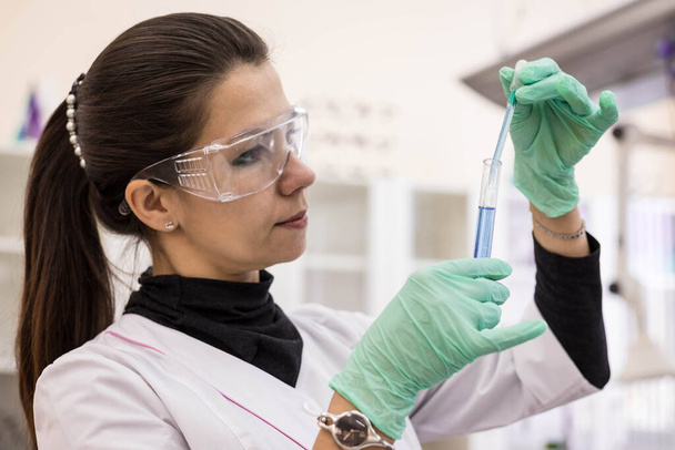 Close-up of a female doctor wearing protective glasses and gloves taking a sample from a test tube for further analysis of the covid test. Covid test in the lab - Foto, Imagem