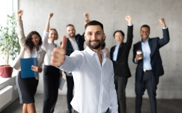 Arabo imprenditore gesturing pollice su standing con dipendenti in ufficio - Foto, immagini