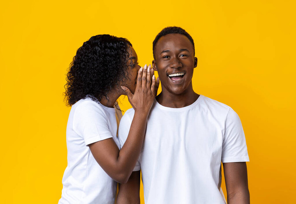 Femme afro-américaine chuchotant quelque chose à son petit ami étonné - Photo, image
