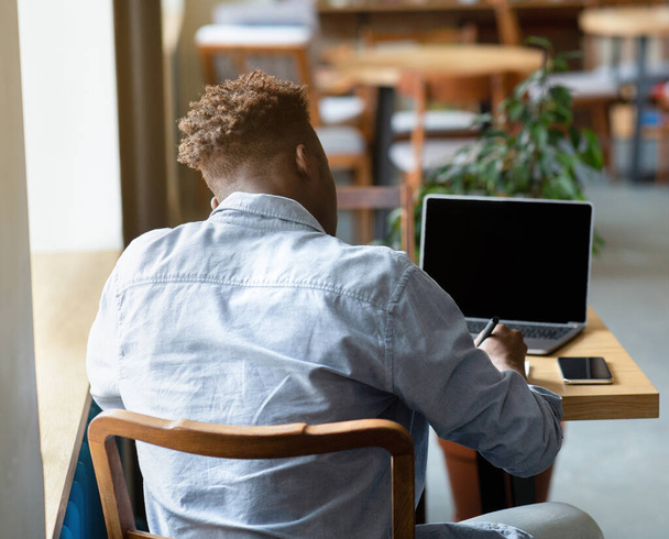 Вид ззаду молодого чорношкірого студента, який навчається онлайн на ноутбуці в міському кафе, макет для дизайну веб-сайту на екрані
 - Фото, зображення