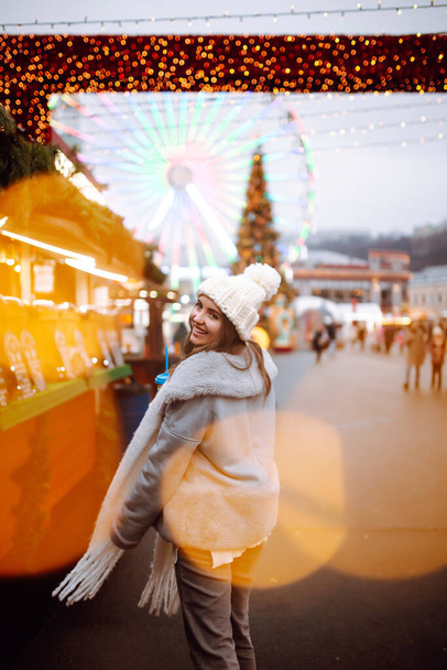 Happy woman  drinking hot coffee in Festive Christmas fair. Beautiful woman enjoys winter holidays on Christmas market. New year.Lights around. - Фото, зображення