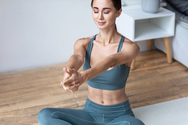 Staying fit and healthy in self-isolation at home. Beautiful young woman in sports clothing doing yoga while relaxing. - Φωτογραφία, εικόνα