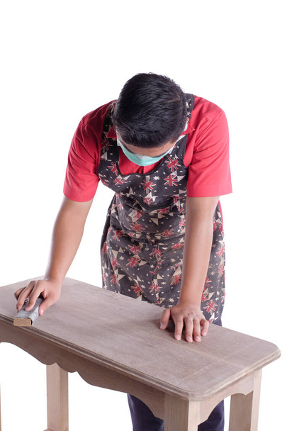 Νεαρός ξυλουργός με ρούχα εργασίας χρησιμοποιώντας γυαλόχαρτο για τη στίλβωση καναπέ server έργο απομονωμένο σε λευκό φόντο - Φωτογραφία, εικόνα