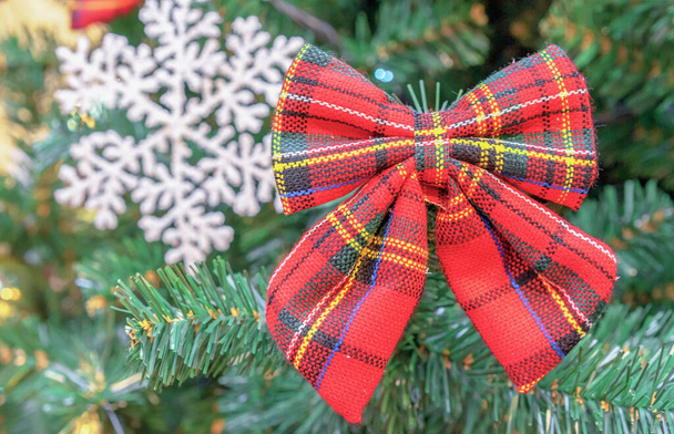 Κόκκινο τόξο με ένα κλουβί Σκωτίας και μια λευκή νιφάδα χιονιού στο χριστουγεννιάτικο δέντρο. - Φωτογραφία, εικόνα