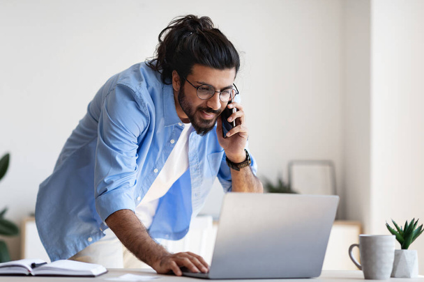 Empreendedor masculino ocidental falando no celular e trabalhando no portátil no escritório - Foto, Imagem