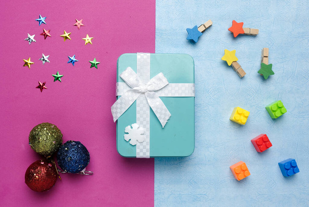 Flachbild einer Aluminium-Geschenkschachtel mit Baustein, Sternen, Weihnachtskugel und Sternen auf rosa und blauem Hintergrund. - Foto, Bild