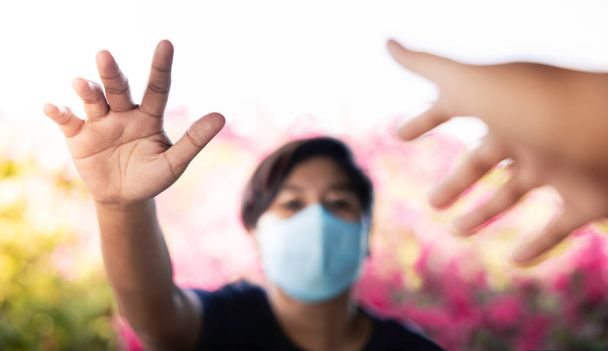 コロナウイルスの概念の間の社会的距離。外科マスクを持つ人は、別のものに触れるために手を上げました。COVID-19中の長距離関係.流行病を止める - 写真・画像