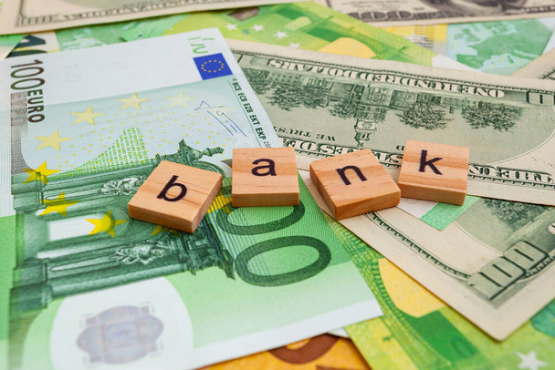 BANK επιγραφή σε ξύλινους κύβους στην υφή μας δολάρια και τραπεζογραμμάτια ευρώ - Φωτογραφία, εικόνα