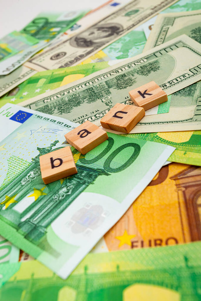 BANK επιγραφή σε ξύλινους κύβους στην υφή μας δολάρια και τραπεζογραμμάτια ευρώ - Φωτογραφία, εικόνα