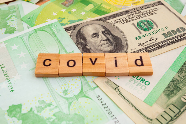COVID19 opschrift op houten blokjes op de textuur van ons dollars en eurobankbiljetten - Foto, afbeelding