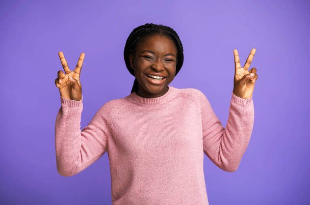 Pokój. Radosna czarna młoda kobieta Gesturing V-Sing i śmiejąc się na fioletowym tle - Zdjęcie, obraz