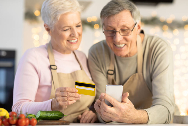 Seniorengattinnen kaufen mit Smartphone und Kreditkarte in Küche ein - Foto, Bild