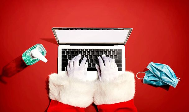 Père Noël utilisant un ordinateur portable avec un masque et une bouteille de désinfectant - Photo, image