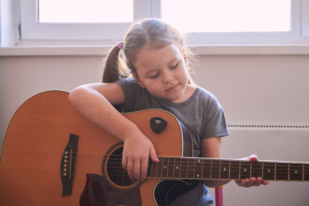 een klein meisje leert gitaar spelen op noten. Muziekschool voor kinderen.Muzieknotatie. - Foto, afbeelding