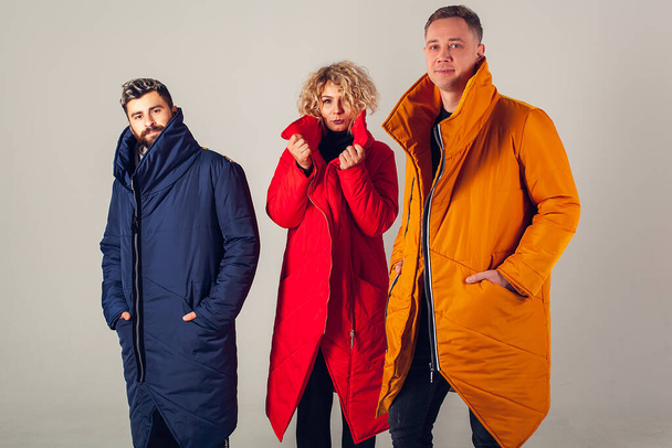 Comfortable winter clothes in different colors on a white background. Three friends with smiles on their faces are dressed in different winter down jackets. The emotion of comfort and convenience on the face. European model appearance. - Foto, afbeelding