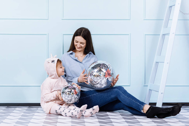 Boldog szerető családot. fiatal anya és kislánya unikornis jelmezben ül a padlón, és játszik disco réteg kék fal háttér. Boldog anyák napját, a baba napját. - Fotó, kép