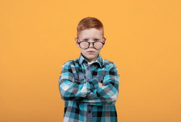 Злий хлопчик в окулярах з обіймами, схрещеними на жовтому
 - Фото, зображення