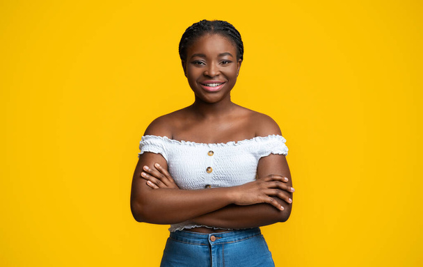Confiant jeune femme afro-américaine debout avec les bras croisés sur fond jaune - Photo, image