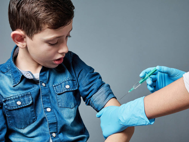 Carino giovane ragazzo vaccinato, si isola su uno sfondo grigio, concetto di vaccinazione - Foto, immagini