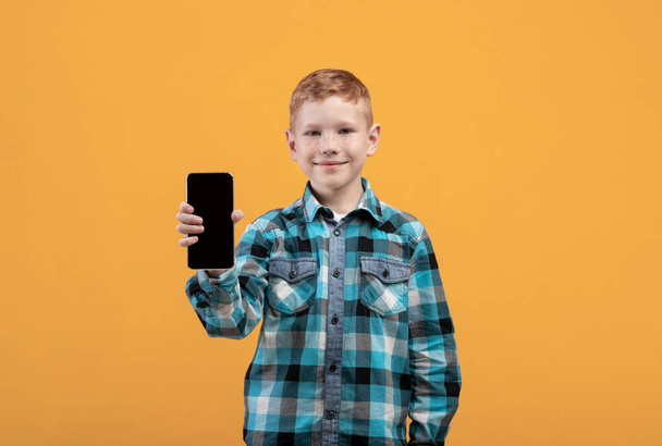 Garçon souriant tenant un téléphone portable avec écran vide - Photo, image