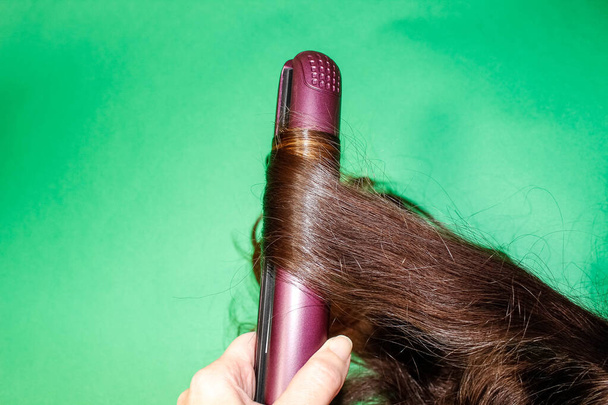 Une mèche de cheveux foncés est enroulée autour d'un Styler chaud. Gros plan. - Photo, image