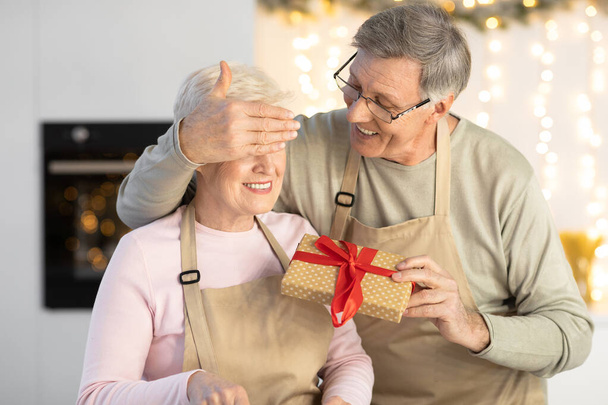 gelukkig leeftijd man verrassende vrouw met kerstcadeau in keuken - Foto, afbeelding