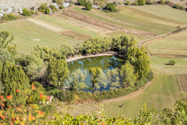 estanque redondo rodeado de árboles en tierras altas verdes, disparado con luz brillante cerca de Calascio, L 'Aquila, Abruzzo, Italia - Foto, Imagen